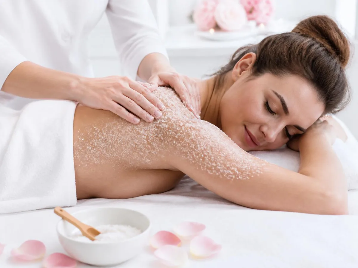 A therapist working a sugar scrub over a relaxed guest’s shoulder and arm